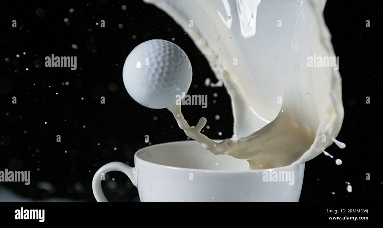 Pallina da golf in una ciotola con latte esplosivo su sfondo nero Foto Stock