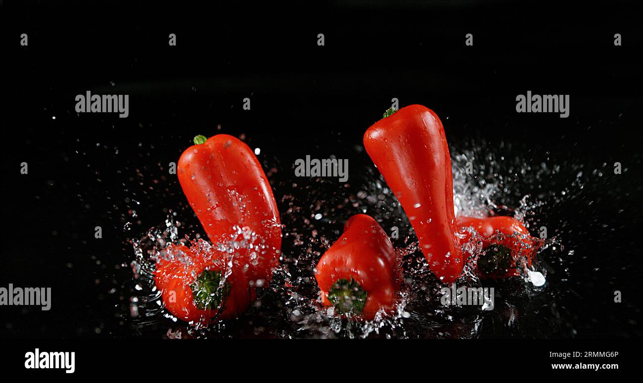 Peperoni rossi dolci, capsicum annuum, verdure che cadono sull'acqua su sfondo nero Foto Stock