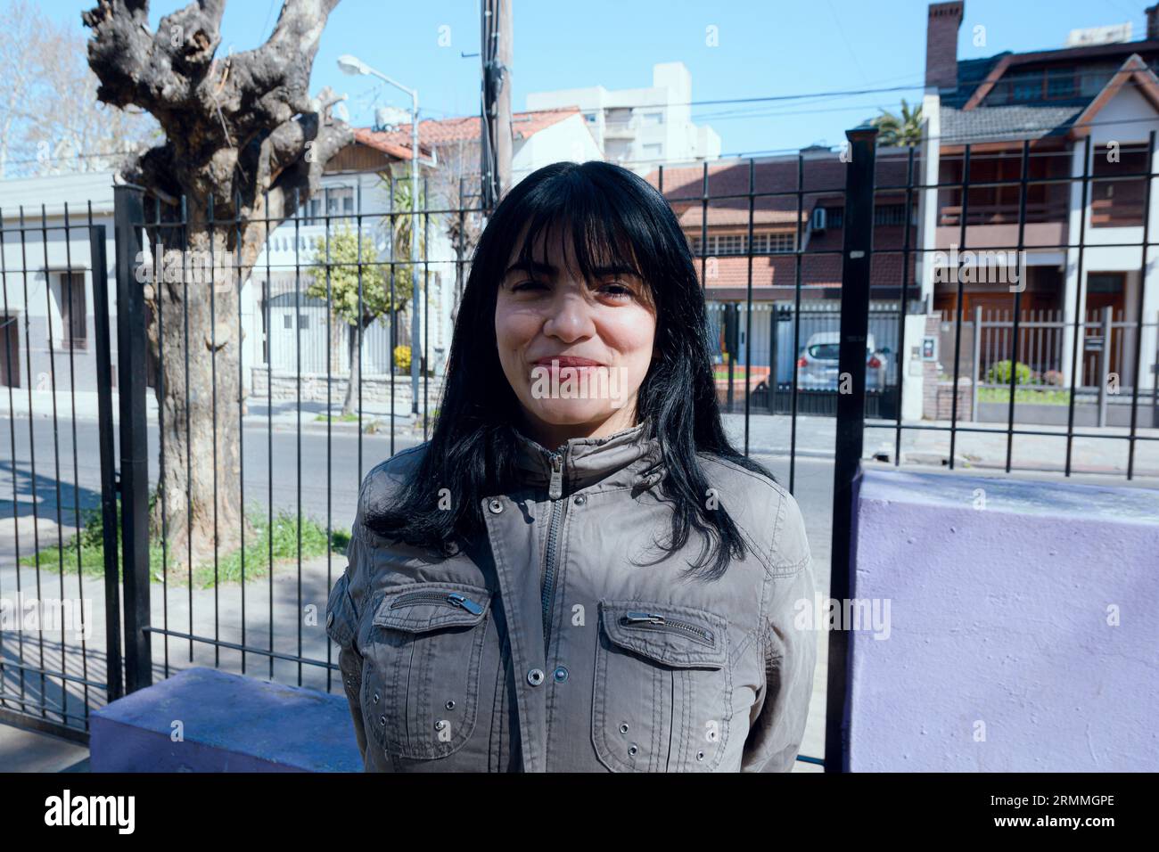 ritratto di timida ragazza latina dai capelli neri venezuelana che indossa una giacca grigia in piedi nel parco guardando la macchina fotografica che tiene indietro il desiderio di ridere, stile di vita Foto Stock