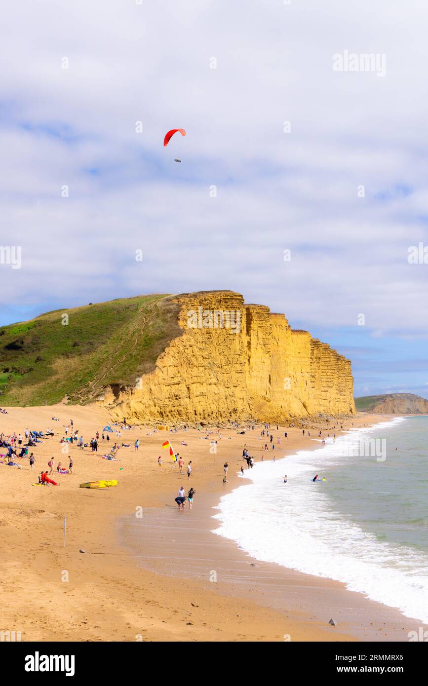 Un parapont che paraponta sulla spiaggia di West Bay Dorset, sulla spiaggia e sulle scogliere, e persone sulla spiaggia in estate; West Bay, Dorset UK Foto Stock