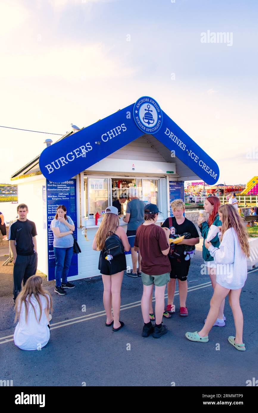 Un gruppo di adolescenti britannici di 13-16 anni che aspettano e mangiano in un fast food all'aperto in una sera d'estate, West Bay, Dorset UK Foto Stock