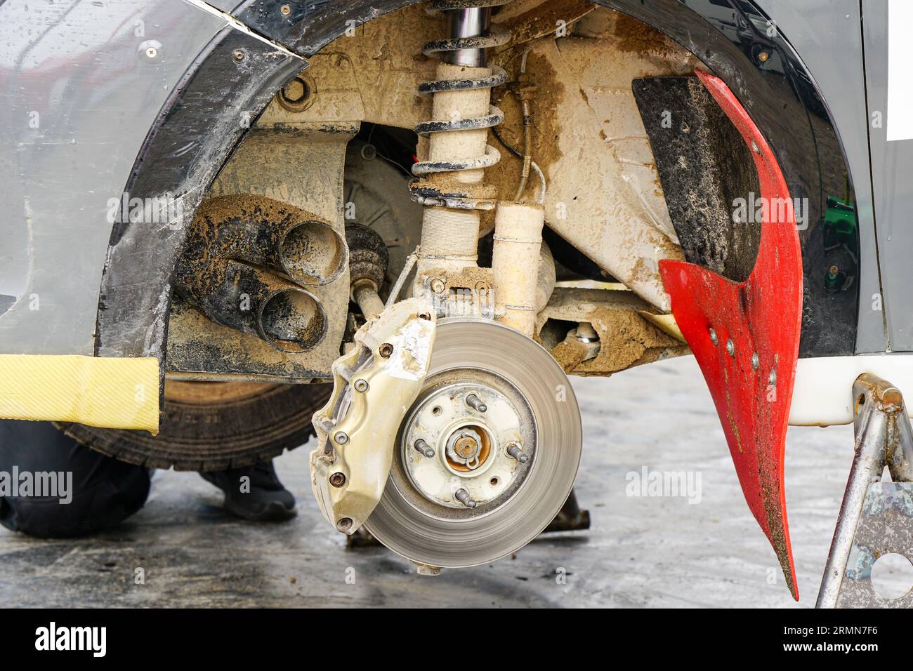 Manutenzione delle vetture da rally nel parcheggio di servizio, ruota rimossa, disco freno con pinza, sospensione fangosa Foto Stock