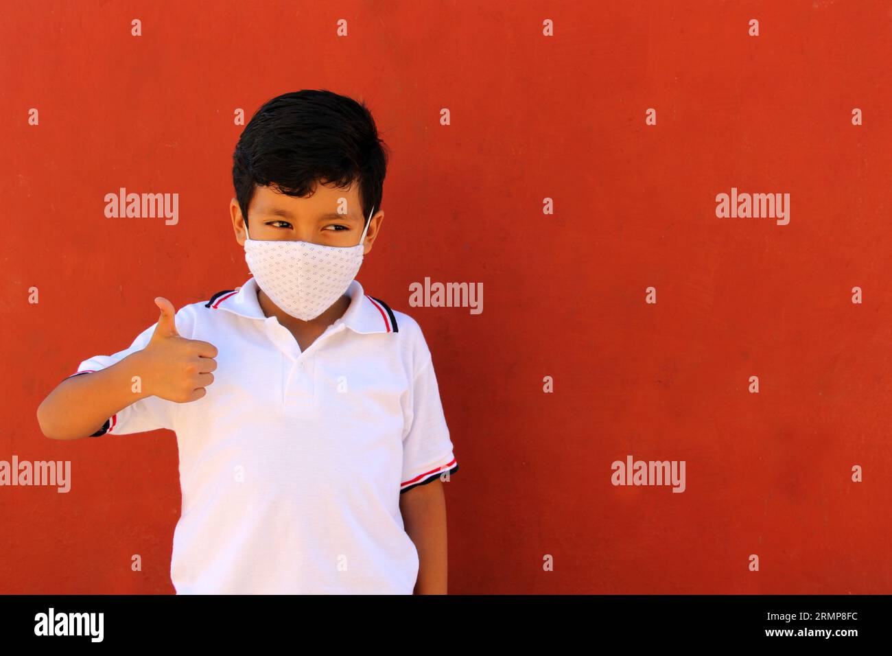 Felice e penoso Latino 8 anni ragazzo che indossa camicia bianca uniforme scolastica e maschera viso per la protezione nella pandemia di Covid-19 al ritorno a scuola Foto Stock