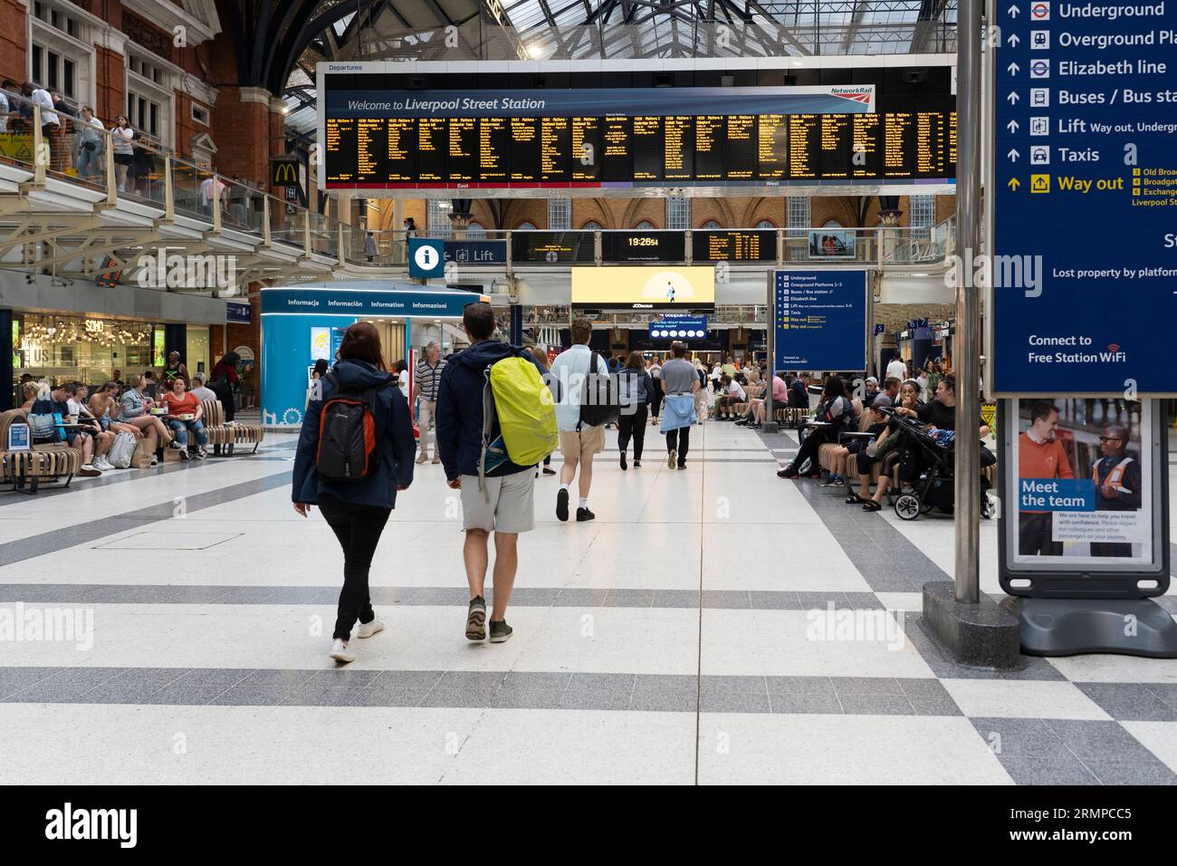 Passeggeri del treno che camminano attraverso la stazione ferroviaria di Liverpool Street con un cartello di benvenuto e orari di partenza del treno con bordo elettronico dietro. Londra, Inghilterra Foto Stock
