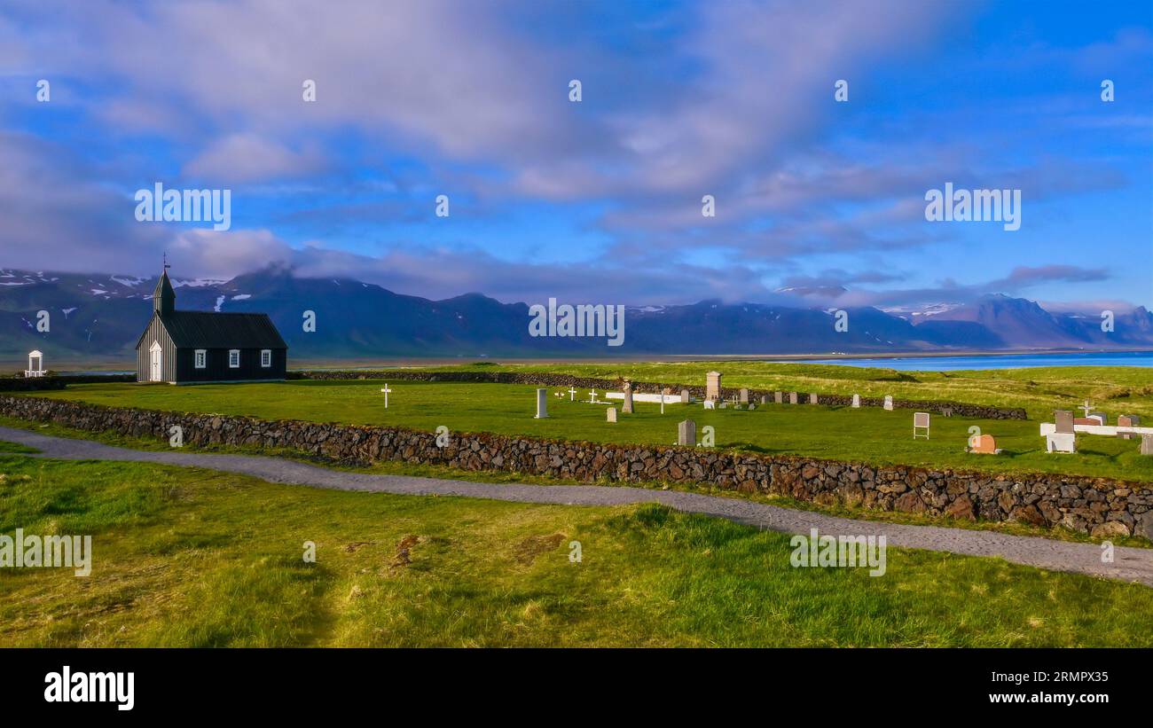 Un'ampia visuale della pittoresca Chiesa Nera di Budir e del suo piccolo cimitero, situato contro montagne e mare, sulla penisola di Snaefellsnes nell'Islanda occidentale. Foto Stock