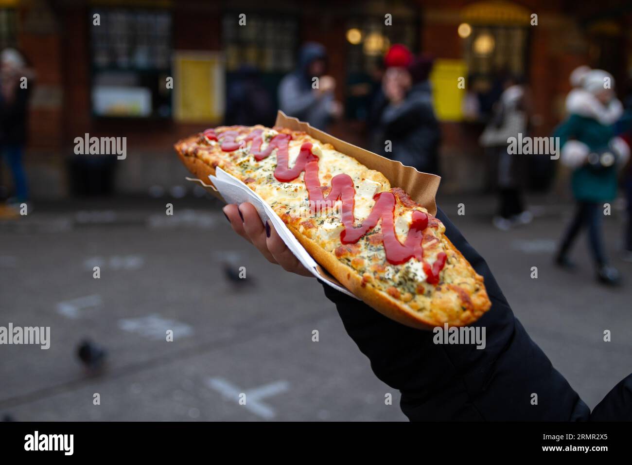 Mano che tiene il panino Zapiekanka a Cracovia, Polonia. Okrąglak Street food Court, Piazza ebraica Plac Nowy, Kazimierz, Kraków, Zapiekanki Krakowskie. Foto Stock