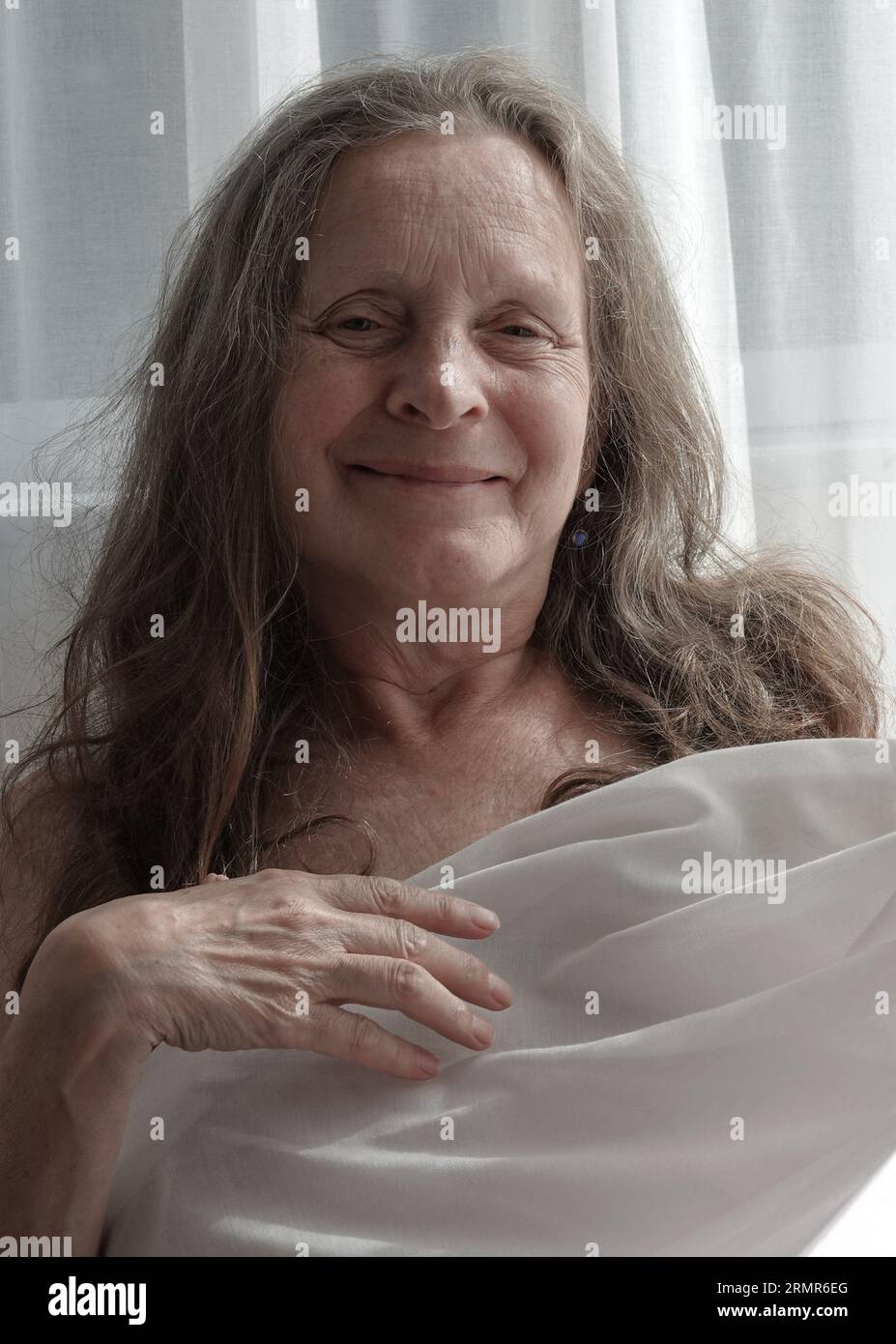 Ritratto di una donna sorridente di 64 anni senza trucco con sfondo chiaro. Foto Stock