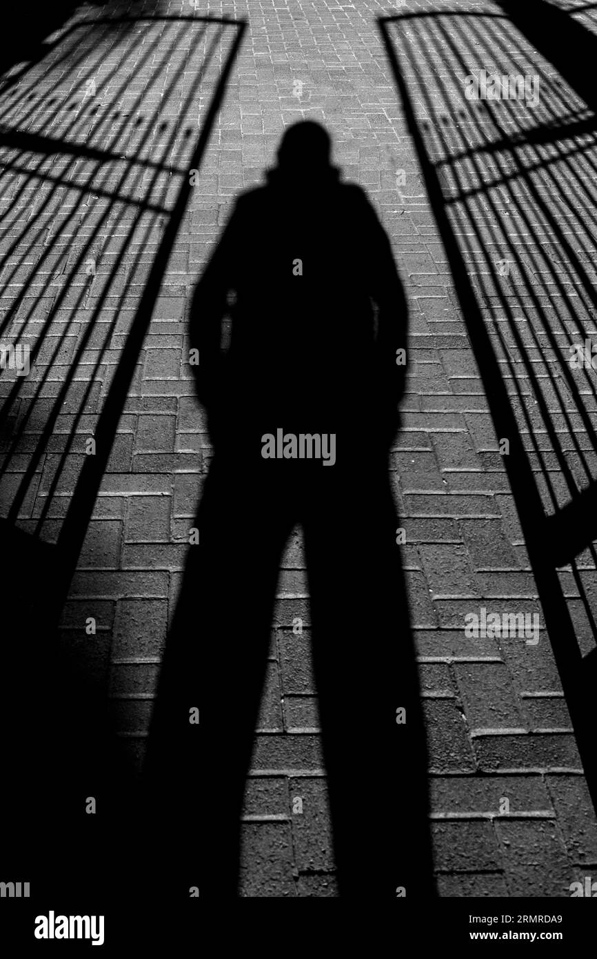 Ombra di persona, gambe separate, in piedi tra due cancelli semi-aperti in ferro battuto Foto Stock