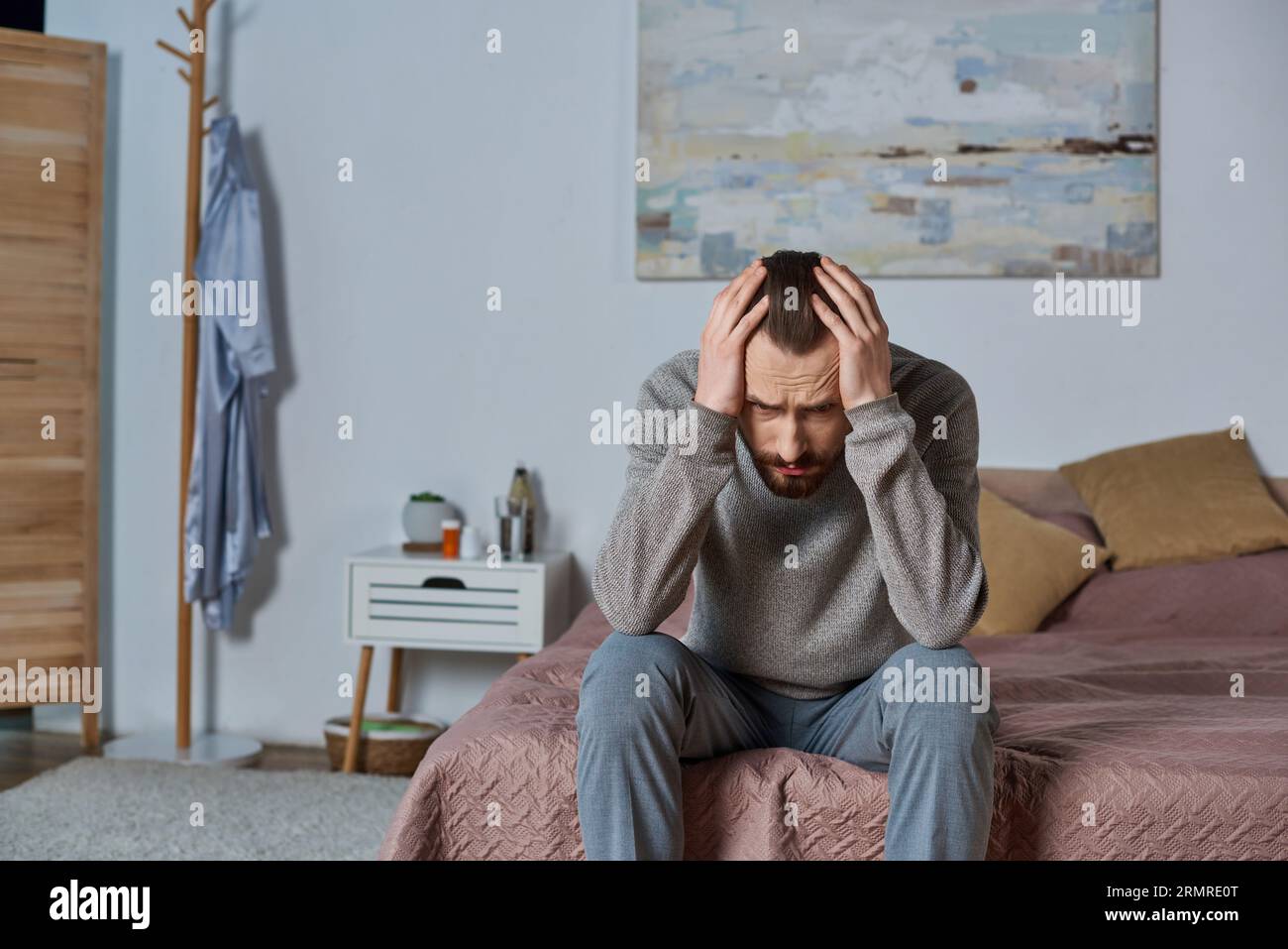 uomo stressato che guarda lontano e seduto sul letto in una camera da letto moderna, dipingendo sulle pareti, solitudine, preoccupazione Foto Stock