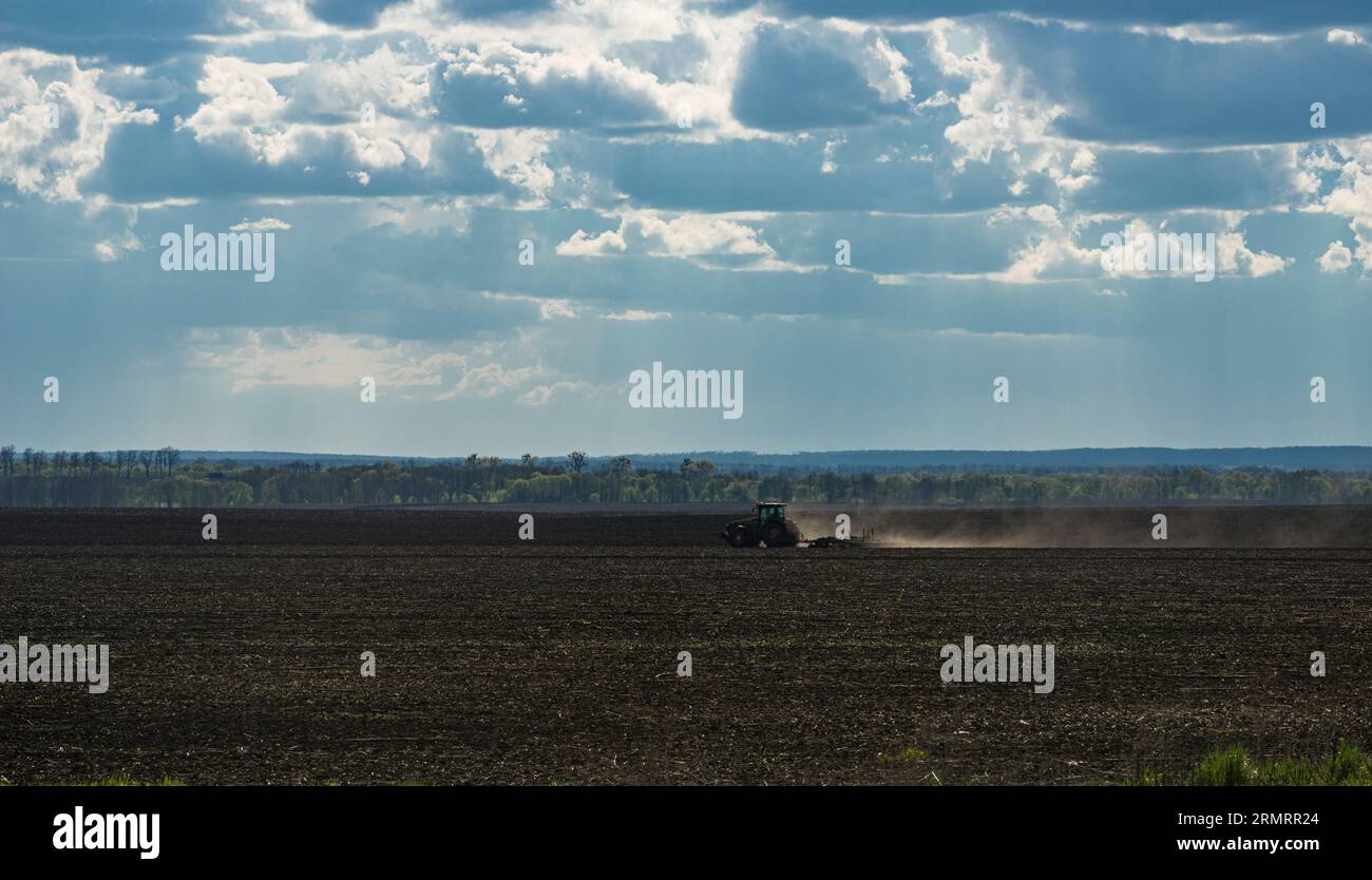 Un campo arato di terreno nero, con un trattore funzionante, in Ucraina Foto Stock