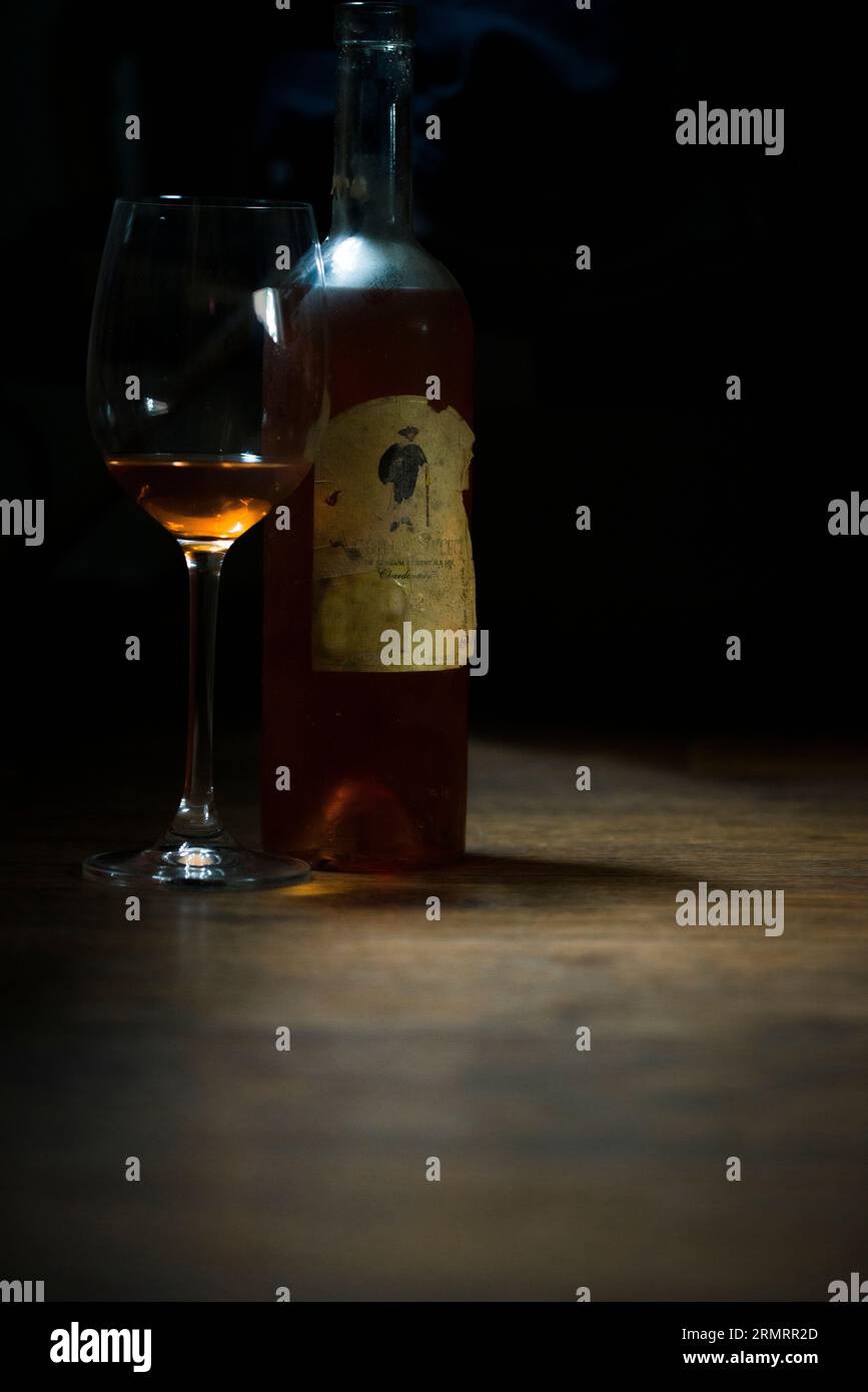 Un bicchiere di vino, e la bottiglia, con un'etichetta, danneggiata con il tempo, nell'invecchiamento in cantina Foto Stock