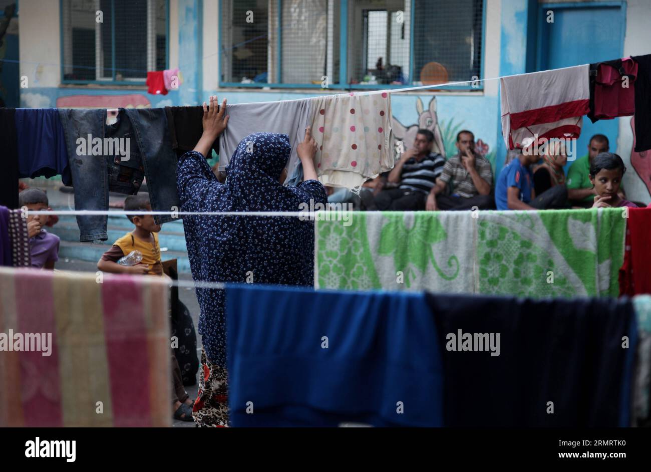 (140803) -- GAZA, 3 agosto 2014 -- Una donna palestinese sfollata impicca vestiti per asciugarsi presso la scuola delle Nazioni Unite Abu Hussein nel campo profughi di Jebaliya, nella striscia di Gaza settentrionale, 3 agosto 2014. Domenica il Presidente palestinese Mahmoud Abbas ha invitato la comunità internazionale a fare pressioni su Israele affinché accetti il cessate il fuoco proposto dall'Egitto nella Striscia di Gaza, ha dichiarato una dichiarazione ufficiale. ) MIDEAST-GAZA-REFUGEE WissamxNassar PUBLICATIONxNOTxINxCHN Gaza 3 agosto 2014 una donna PALESTINESE sfollata impicca i vestiti per asciugarsi PRESSO la scuola delle Nazioni Unite Abu Hussein nel campo profughi di Jebaliya nella striscia di Gaza settentrionale 3 agosto 2014 preside PALESTINESE Foto Stock