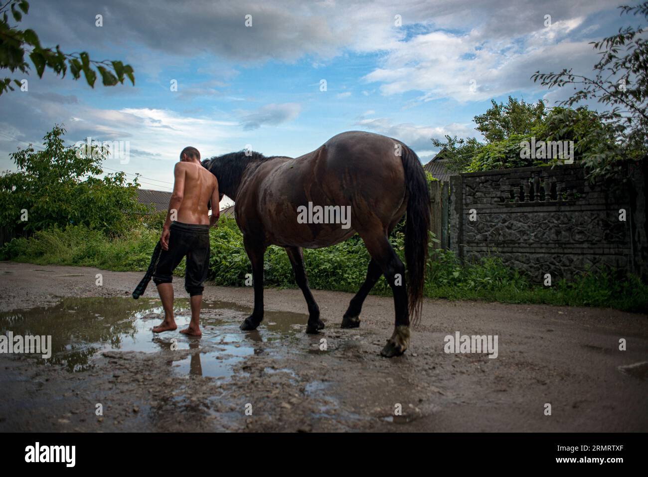 Uomo bagnato mezzo nudo, con il suo cavallo, vicino a una pozzanghera, dopo il temporale Foto Stock
