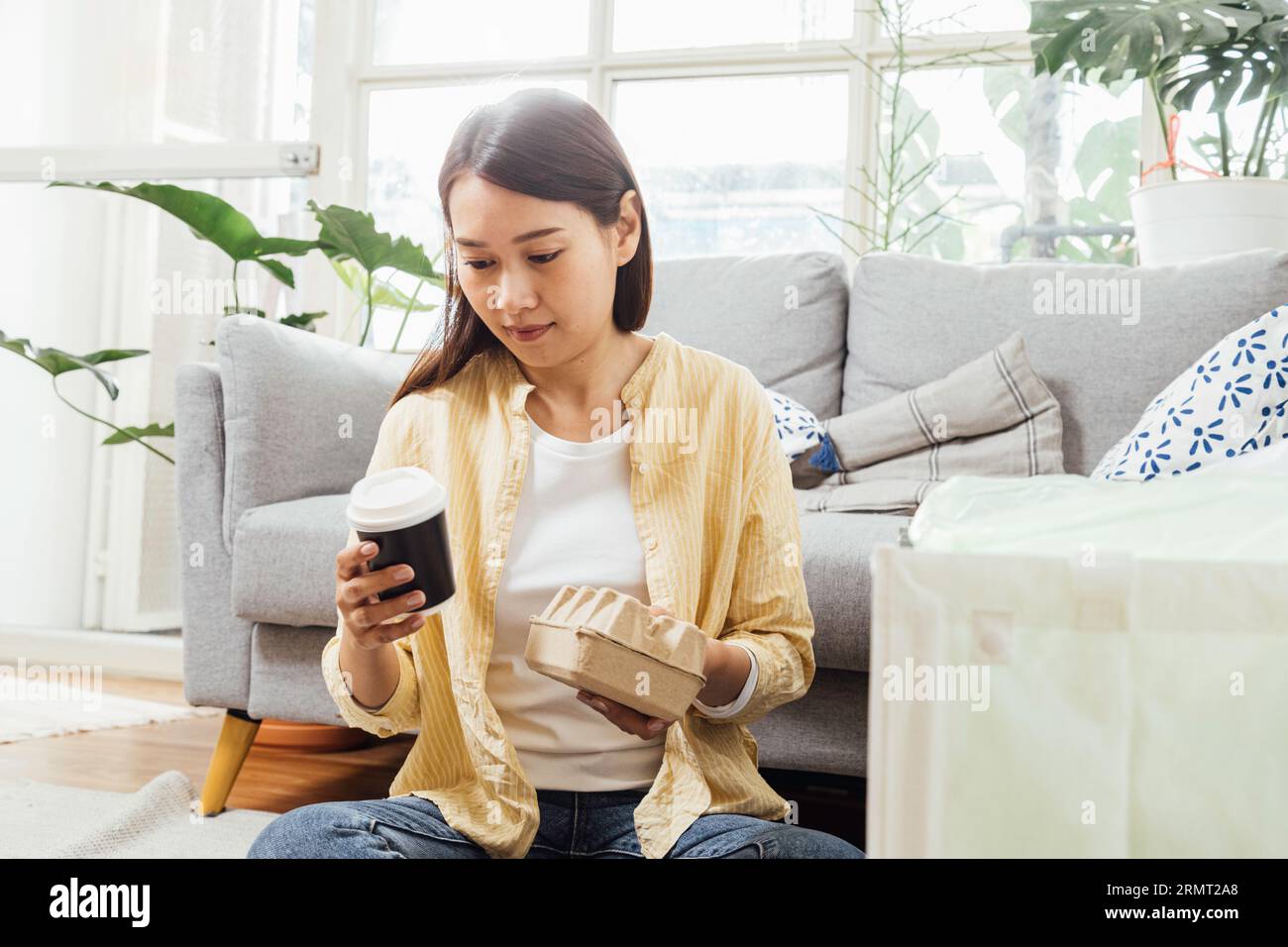 Donna asiatica spazzatura separata a casa. giovane donna che smista e ricicla plastica, carta, lattine in alluminio e contenitori per alimenti per cestini nel soggiorno Foto Stock