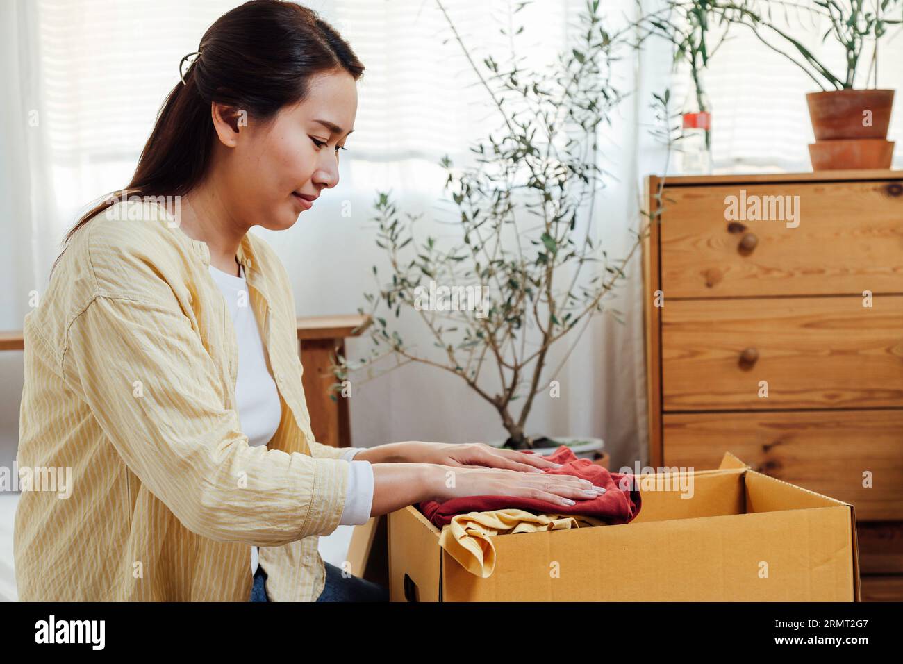 volontaria donna asiatica che mette vestiti inutilizzati in scatole di cartone per donazioni e beneficenza. Concetto di riutilizzo, riciclo, rinnovabile e sostenibilità. Foto Stock