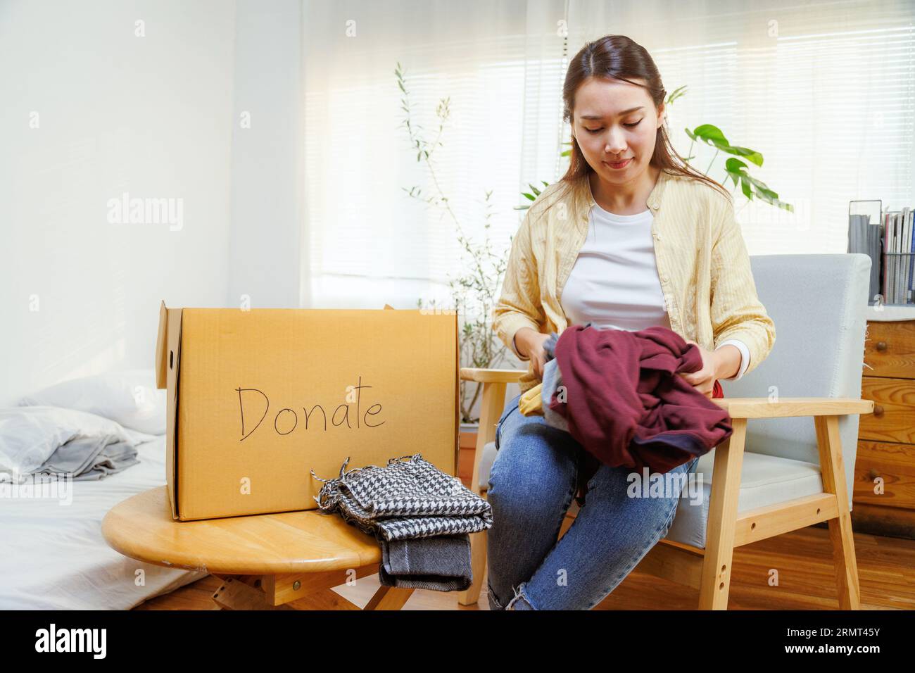 volontaria donna asiatica che mette vestiti inutilizzati in scatole di cartone per donazioni e beneficenza. Concetto di riutilizzo, riciclo, rinnovabile e sostenibilità. Foto Stock