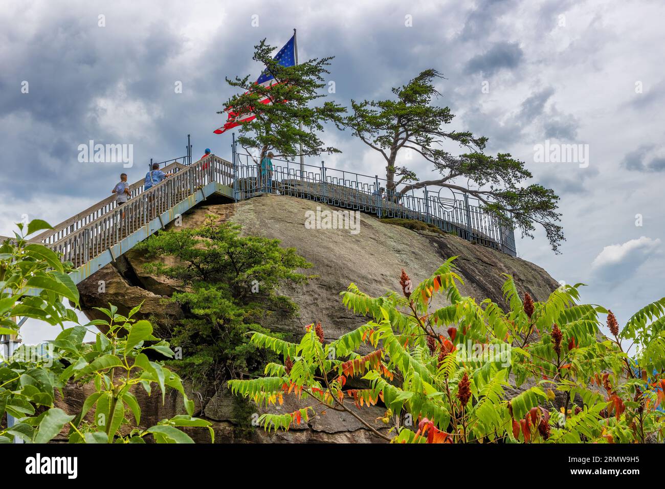 Chimney Rock, North Carolina, USA - 11 agosto 2023: Vista sopra la cima di Chimney Rock, dove vola la bandiera americana e la gente sale le scale Foto Stock