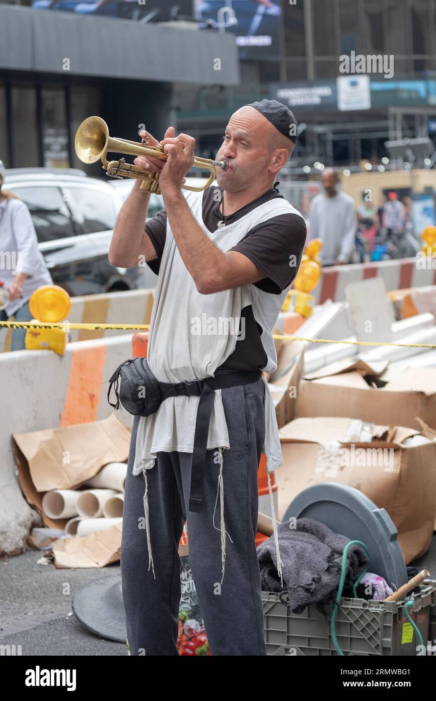 Un uomo ebreo che indossa un cappello e uno tzitzits suona la tromba sulla 8th Avenue e sulla 34th Street a Manhattan, New York City. Foto Stock