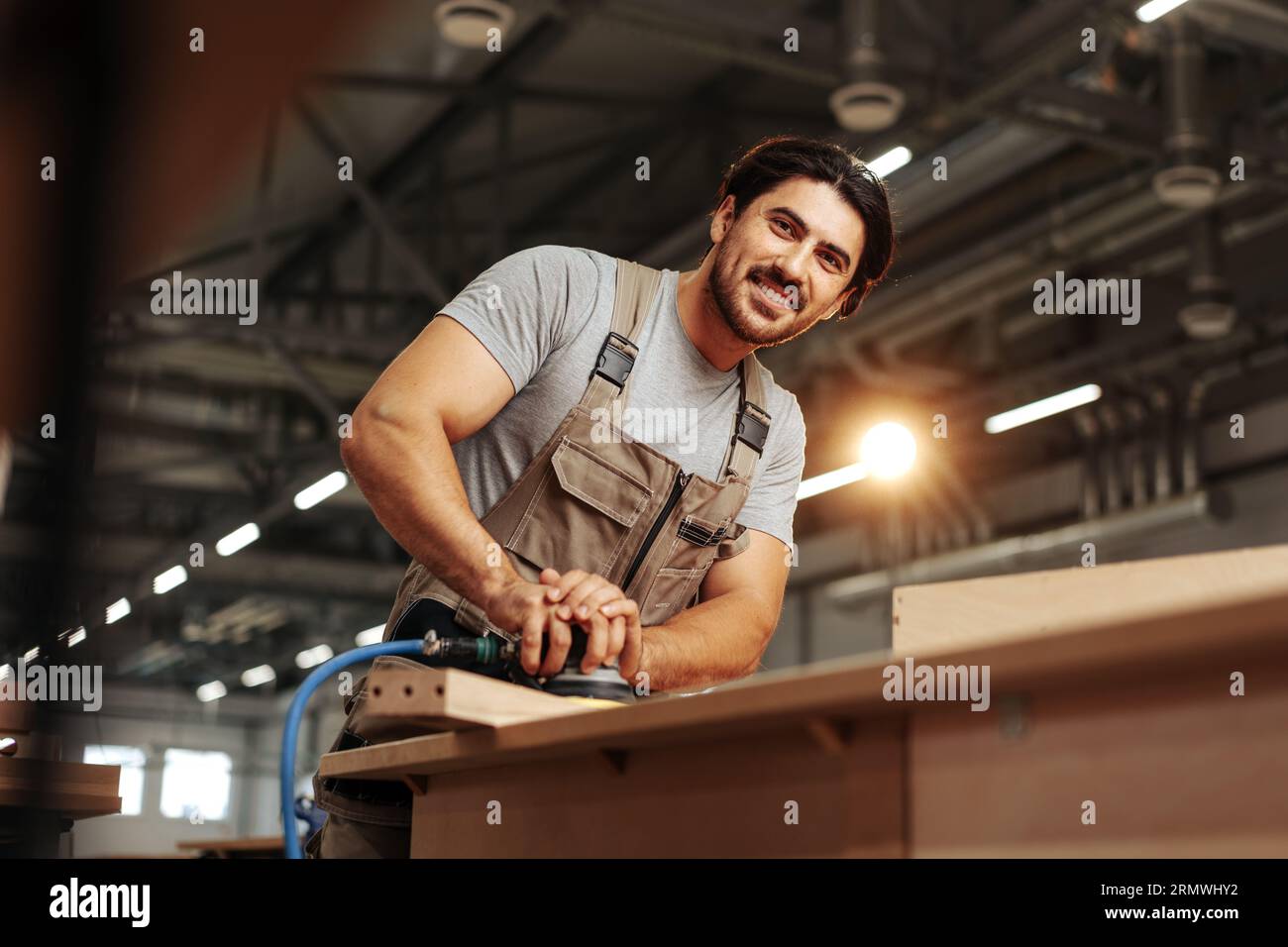 Giovane falegname che levigava il pezzo di legno in officina nella fabbrica di mobili Foto Stock