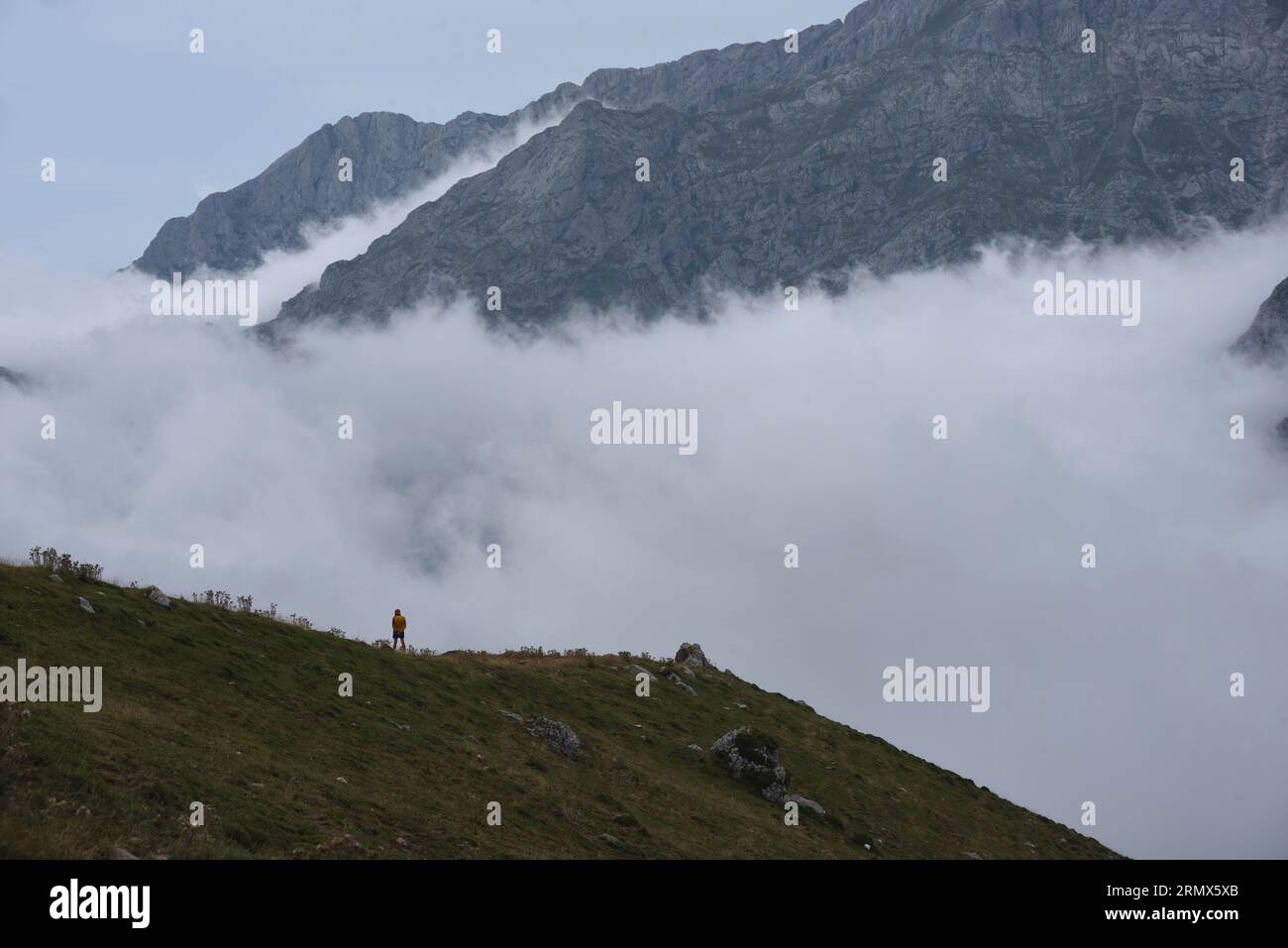 Il massiccio orientale dei Picos de Europa, nel nord della Spagna, dal Puertos de Aliva, con nubi che nascondono i pendii inferiori. Un camminatore solitario fornisce la bilancia Foto Stock