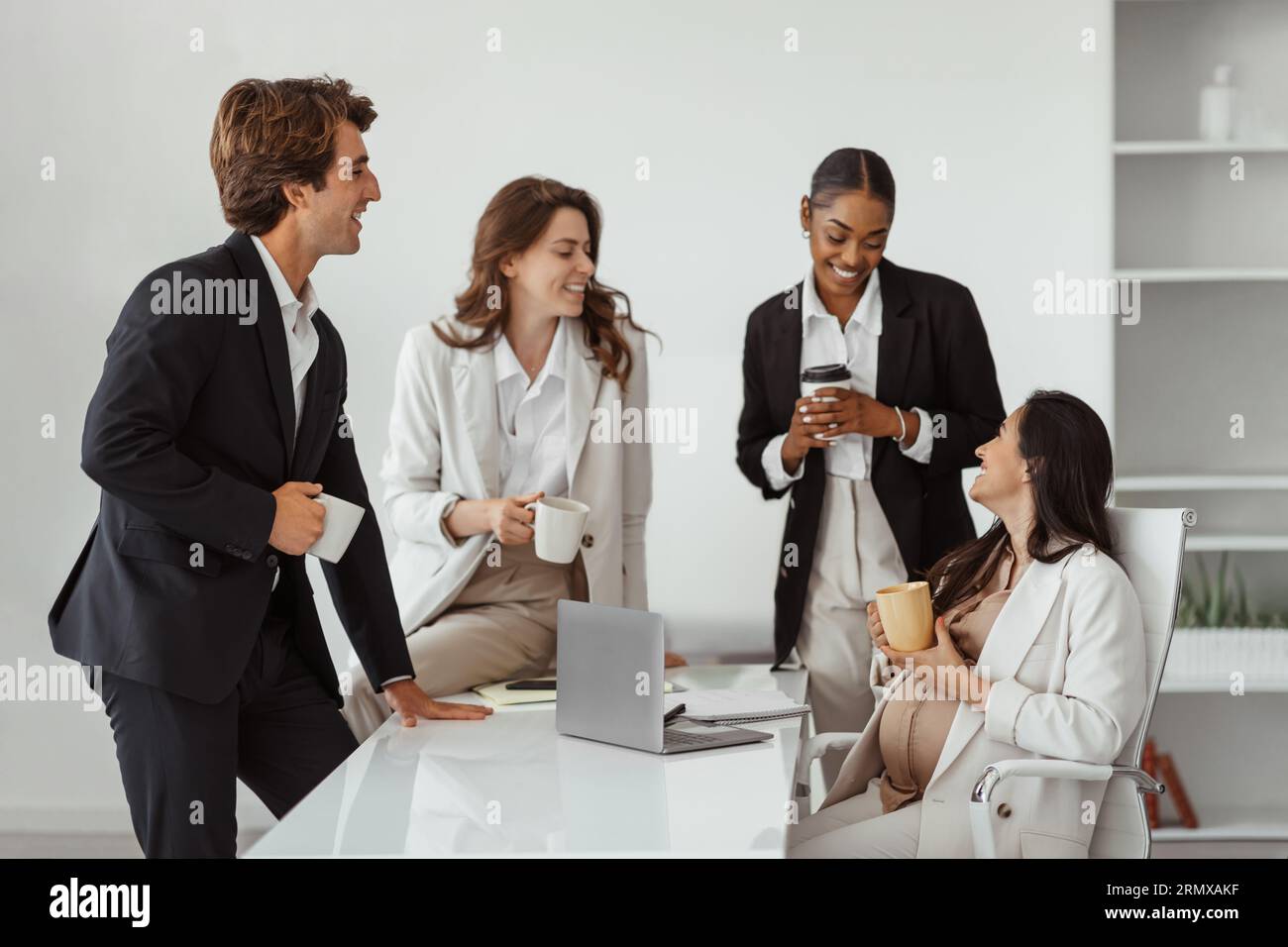 Felice donna in attesa latina che parla con i suoi colleghi d'affari multirazziali mentre fa una pausa in un ufficio moderno Foto Stock
