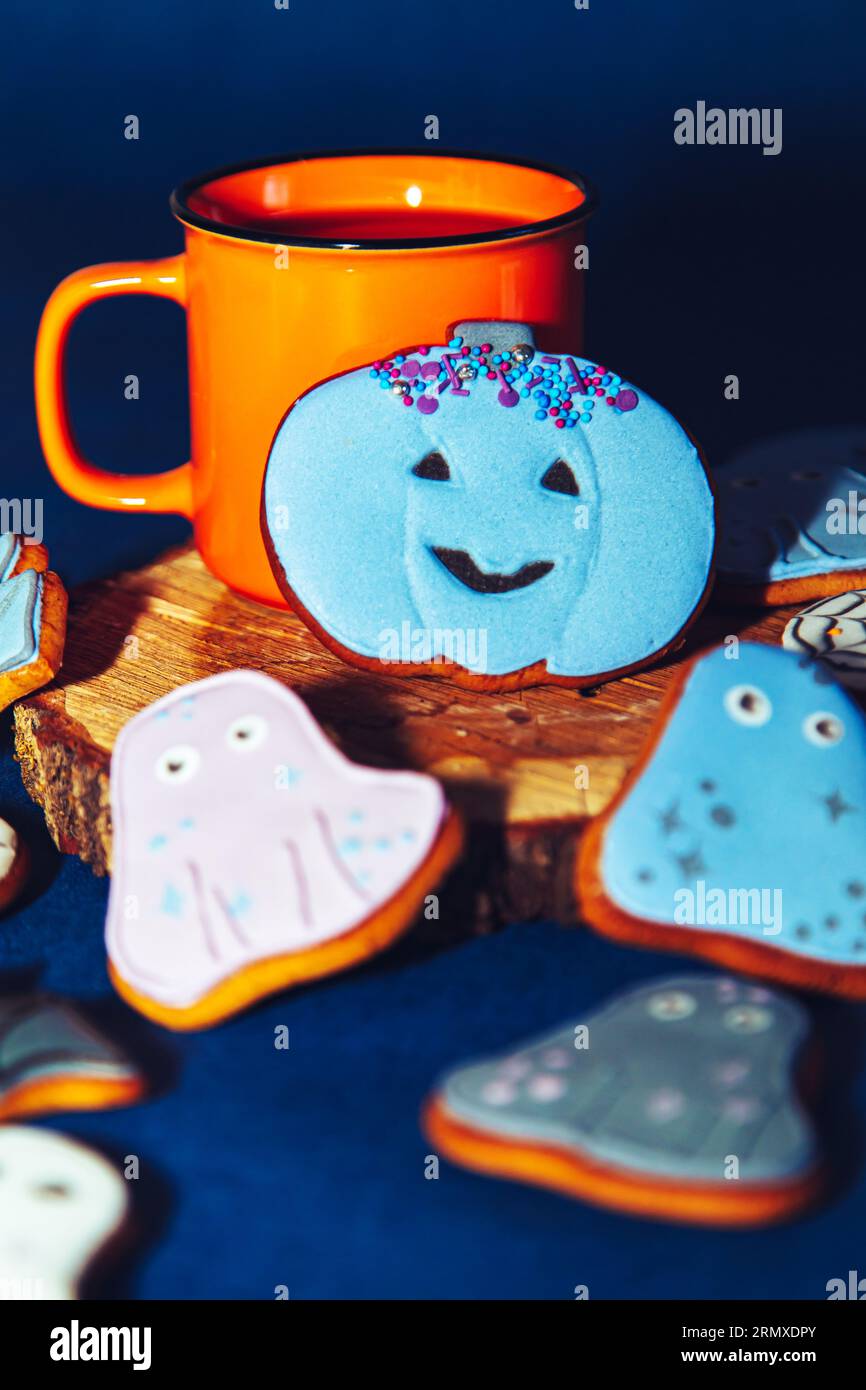 Biscotti di Halloween dipinti con pan di zenzero e una tazza arancione su sfondo blu. Sfondo gastronomico di Halloween. Foto Stock