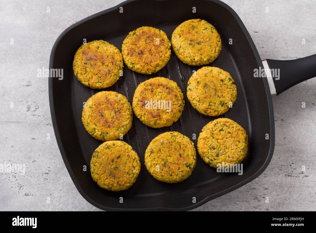 Cotolette di miglio vegano con carote, verdure e semi in padella su sfondo grigio testurizzato, vista dall'alto. Piatti vegani fatti in casa. Foto Stock