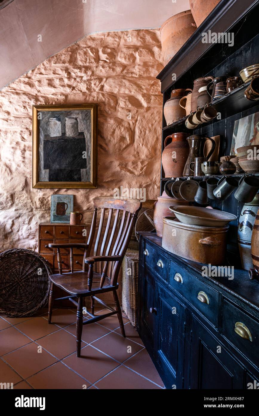 Ceramiche sul comò da cucina sono state messe in risalto con una vecchia sedia di legno. Conversione di loft di fiori del XVIII secolo vicino a Penzance in Cornovaglia, Regno Unito Foto Stock