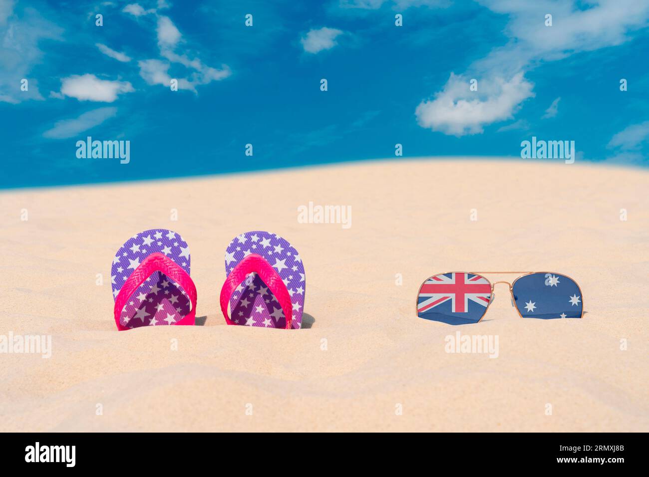 Gli occhiali da sole con occhiali sotto forma di bandiera dell'Australia e infradito giacciono sulla sabbia contro il cielo blu. Concetto di vacanze estive e viaggi in Australia Foto Stock