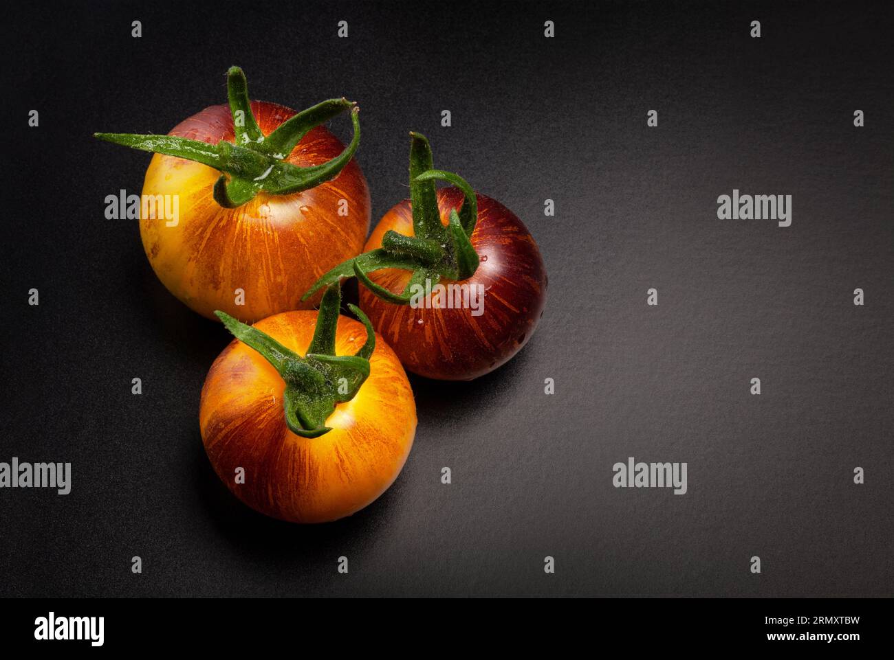 Pomodori a strisce rosse gialle bagnati su fondo nero Foto Stock