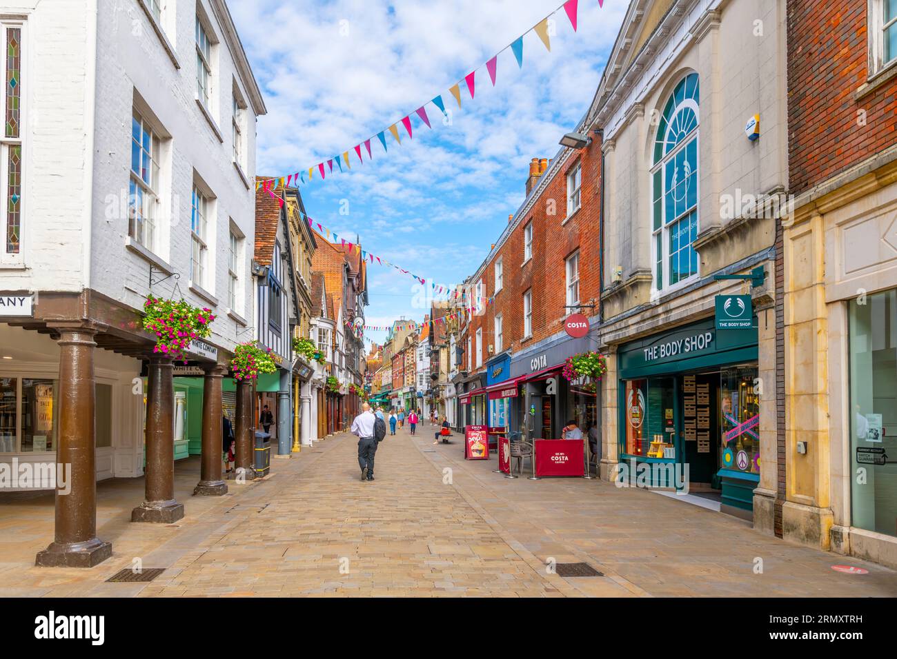 Negozi, caffè e pub lungo il marciapiede costeggiano il principale quartiere commerciale di High Street nella storica città medievale di Winchester, Inghilterra, Regno Unito. Foto Stock