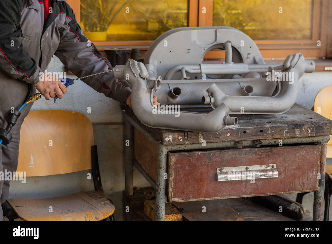 Man sta usando una pistola ad aria compressa per pulire le parti dell'auto dalla sabbia che sono state appena sabbiate prima del restauro. Pulizia del pa automatico sabbiato Foto Stock