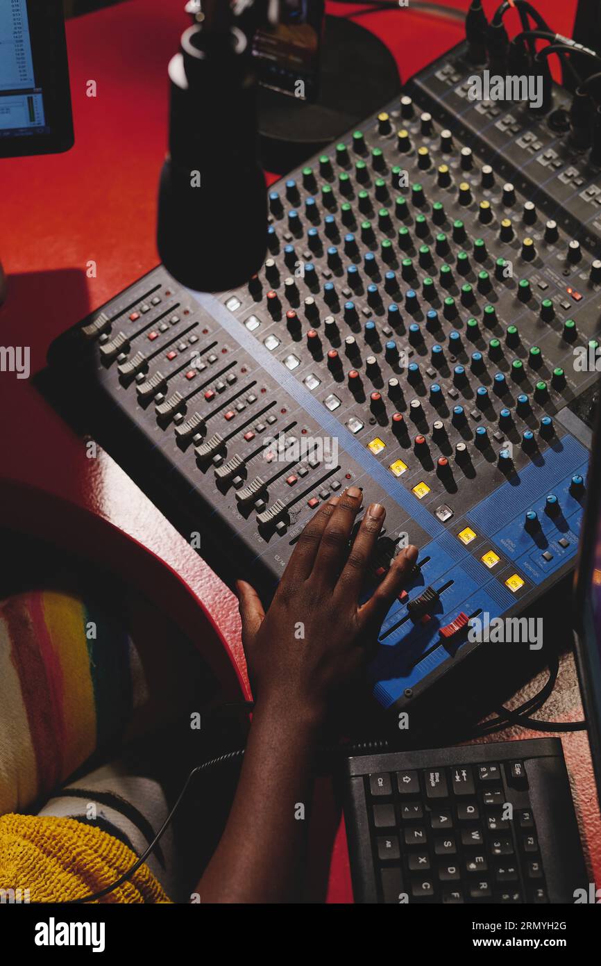 Dall'alto del Ritaglia host radio etnico anonimo che controlla la console di mixaggio con i pulsanti mentre si è seduti al tavolo in studio di trasmissione Foto Stock