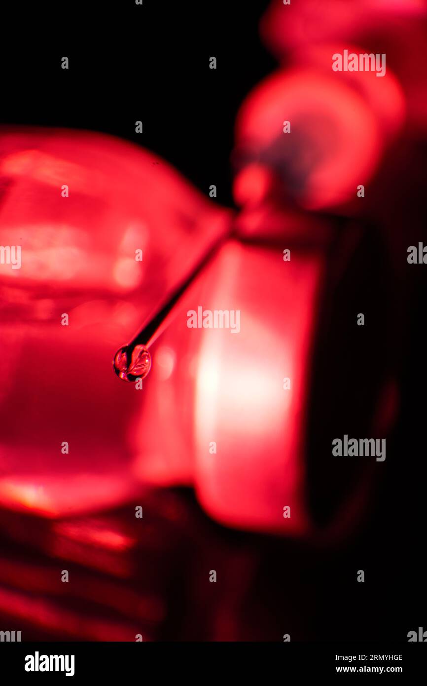 Concentrarsi sulla goccia di vaccino alla punta dell'ago posta su una fiala di vetro alla luce rossa su sfondo nero Foto Stock
