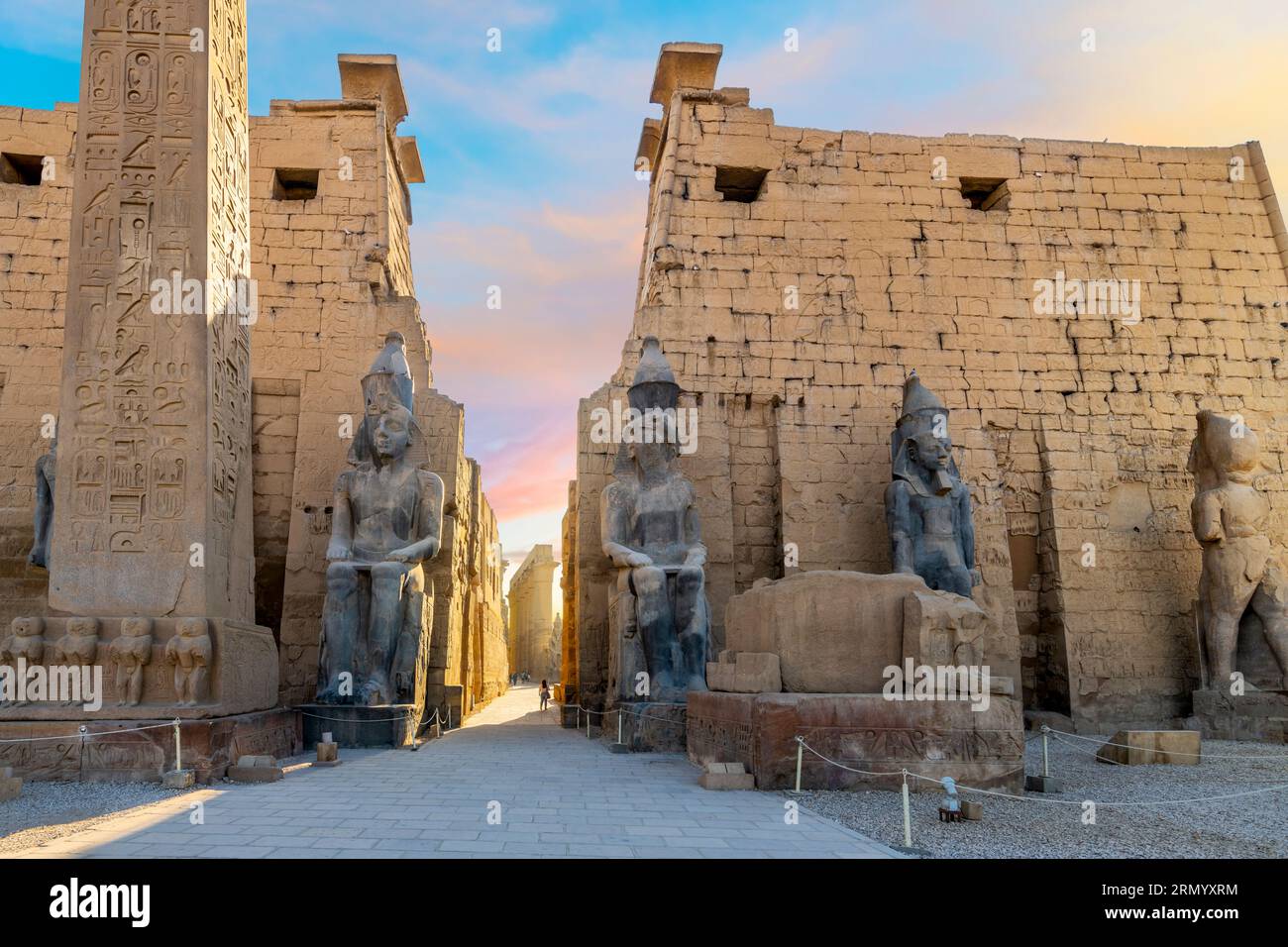Ingresso all'antico tempio egizio di Luxor con statue di Ramses II e l'obelisco del pilone mentre il sole si trasforma nei colori vicino al tramonto a Luxor, in Egitto. Foto Stock