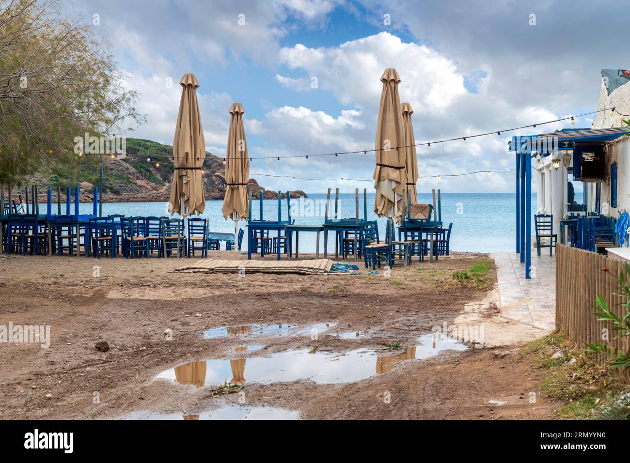 Un caffè all'aperto sul mare chiuso con tavoli e sedie blu impilati, in una giornata di pioggia d'autunno sovrastata lungo la costa di Capo Sunio, Grecia. Foto Stock