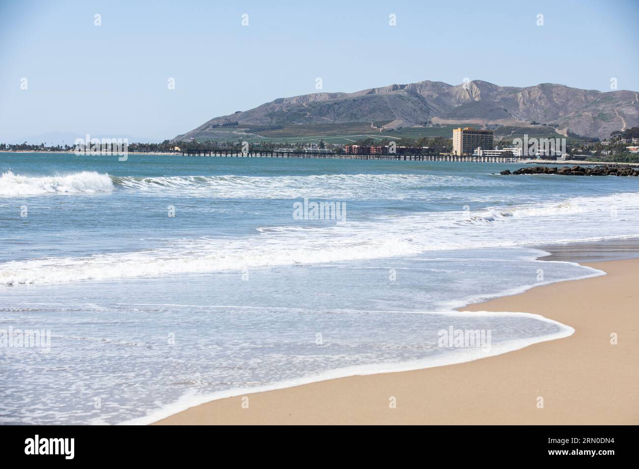 Le onde si infrangono lungo Ventura Beach con lo skyline del centro di Ventura, California, USA sullo sfondo. Foto Stock