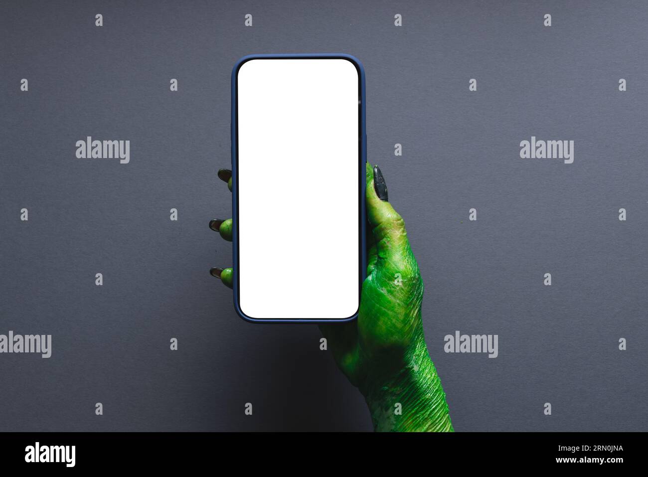 Mano mostro verde che regge lo smartphone con spazio per la copia su sfondo grigio Foto Stock