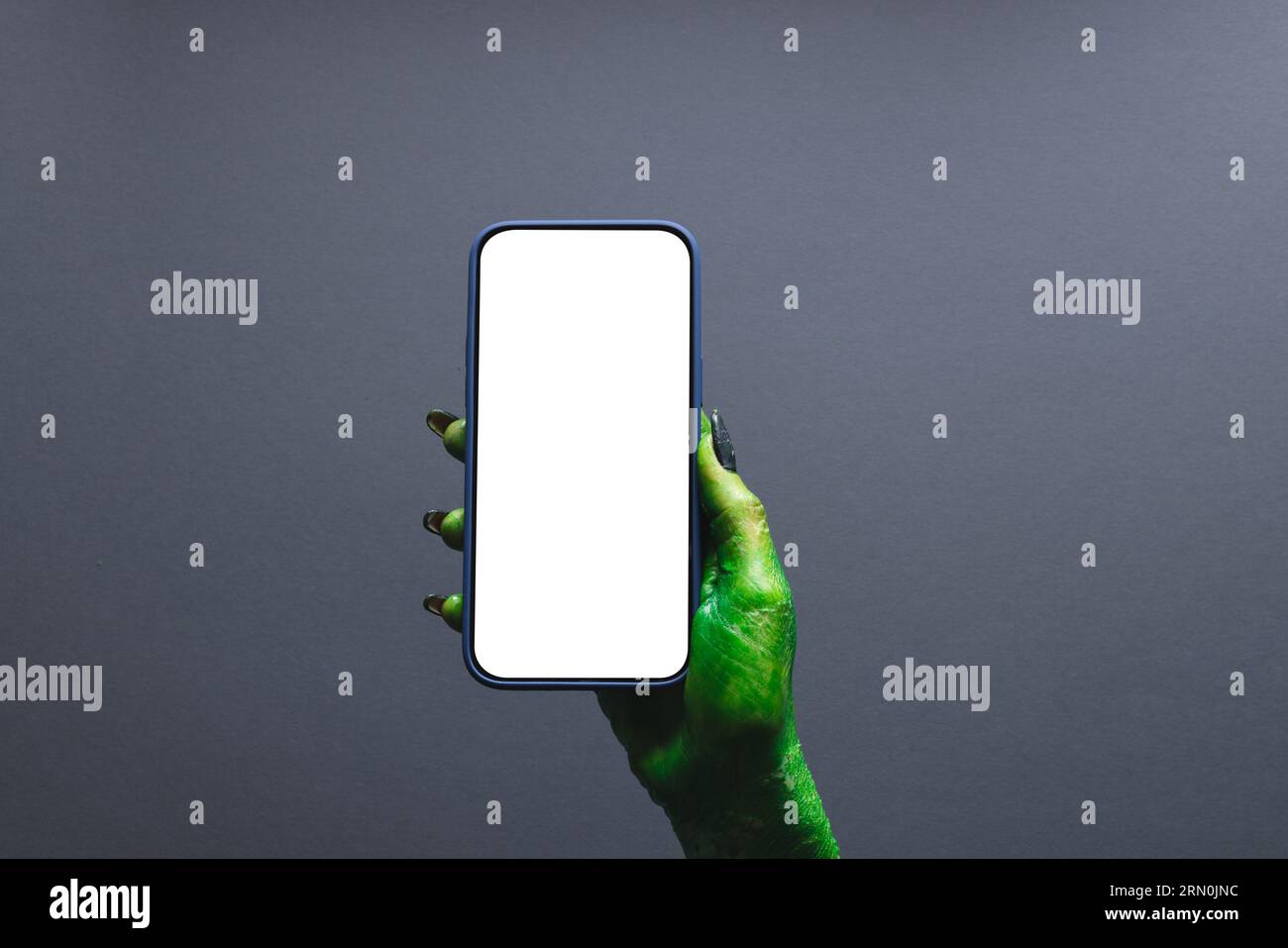 Mano mostro verde che regge lo smartphone con spazio per la copia su sfondo grigio Foto Stock