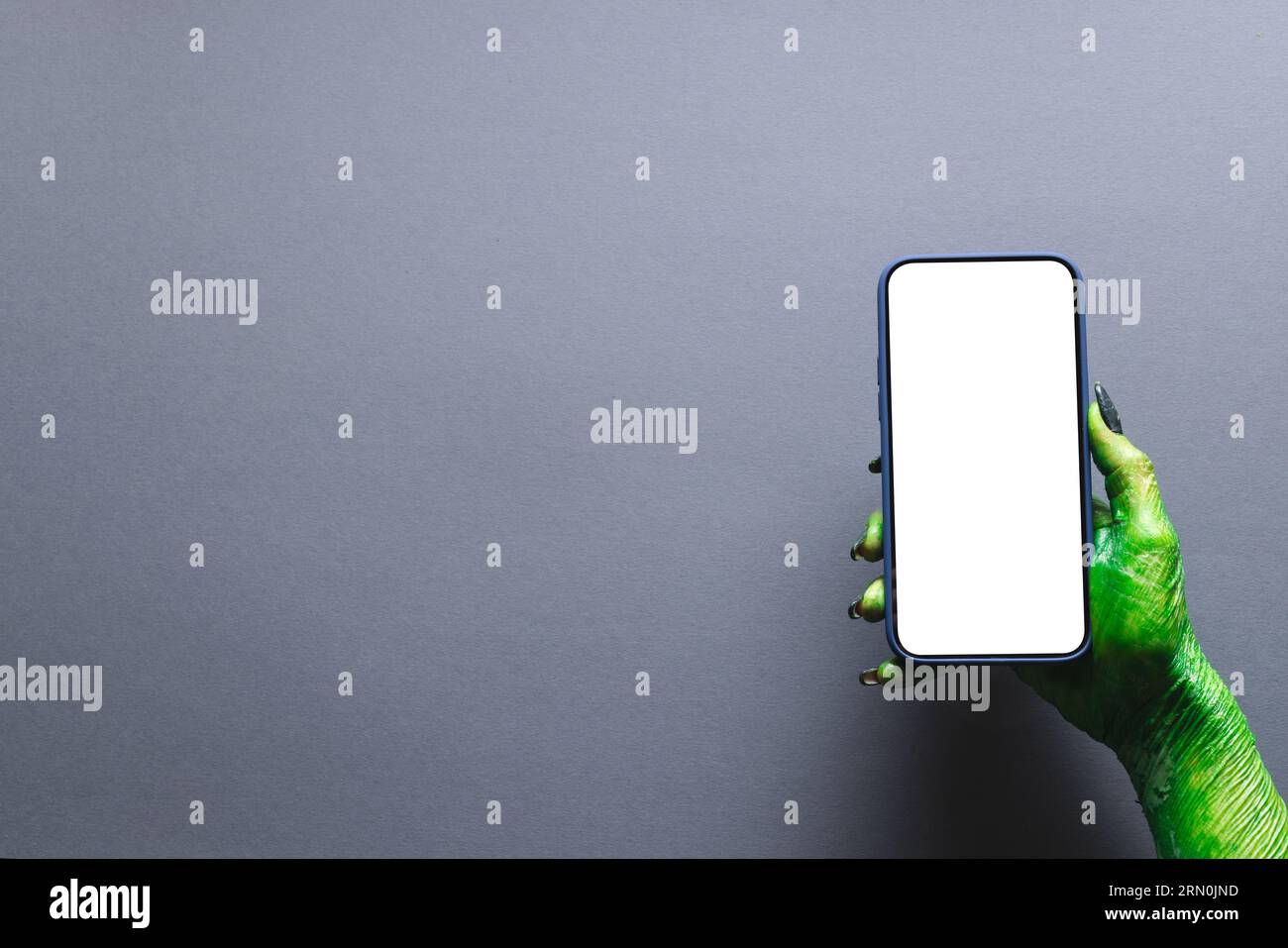 Mano mostro verde che regge lo smartphone con spazio per la copia su sfondo grigio Foto Stock