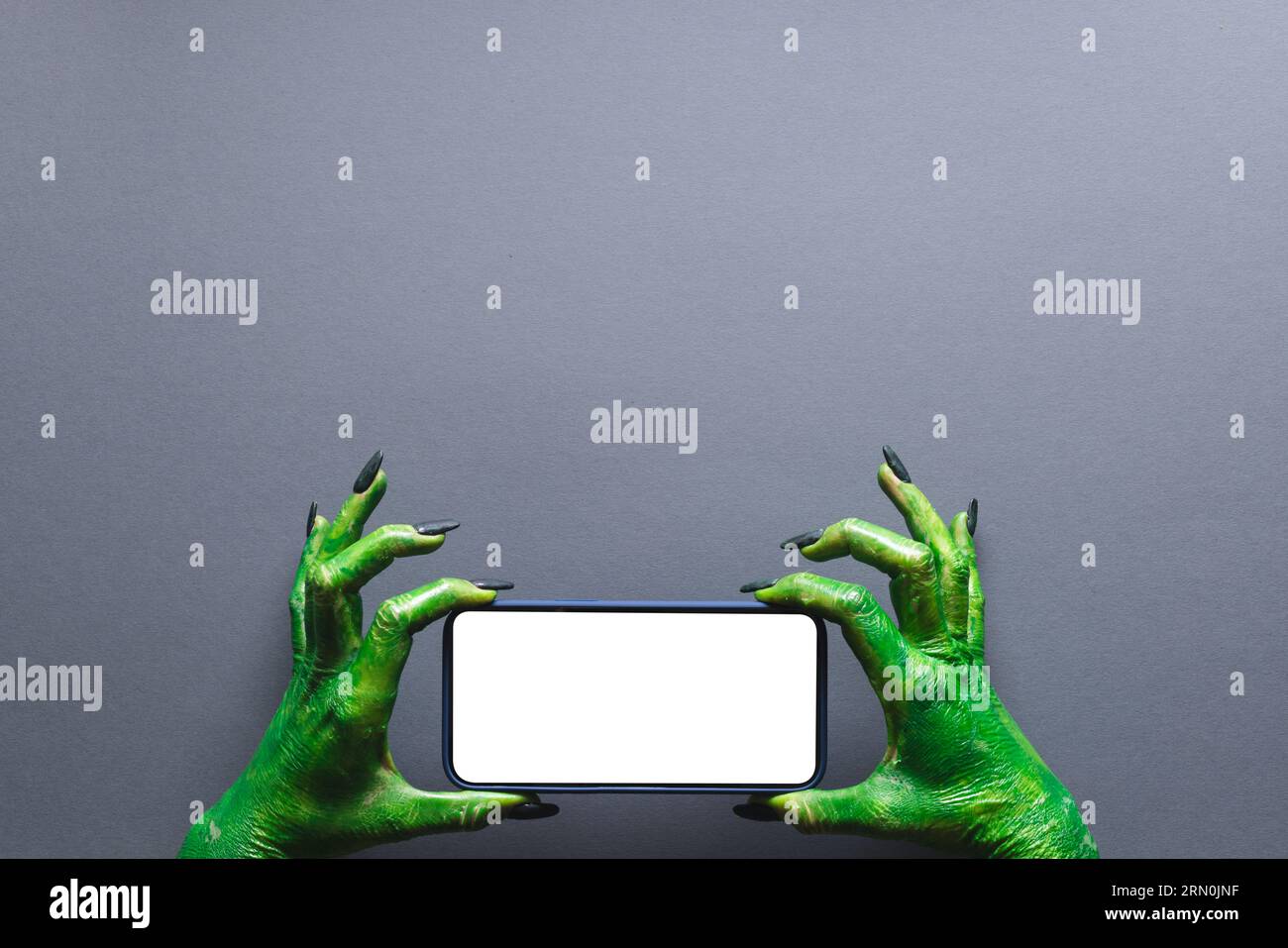 Lancette verdi che reggono lo smartphone con spazio per la copia su sfondo grigio Foto Stock