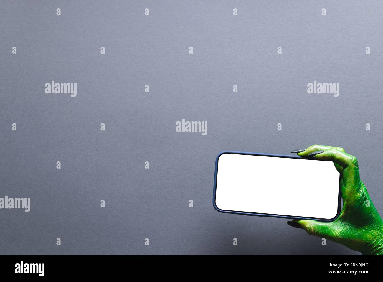 Mano mostro verde che regge lo smartphone con spazio per la copia su sfondo grigio Foto Stock