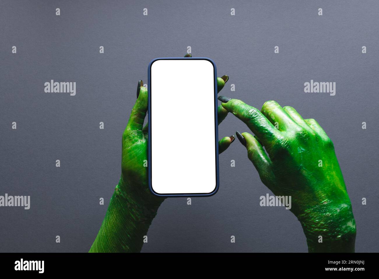 Mano mostro verde che regge lo smartphone con spazio per la copia su sfondo grigio Foto Stock