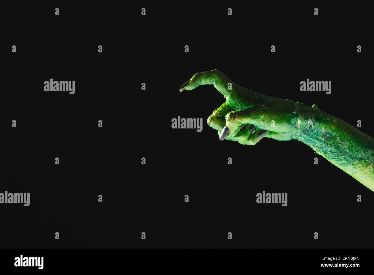 Mano mostro verde con unghie nere che puntano con il dito su sfondo nero Foto Stock