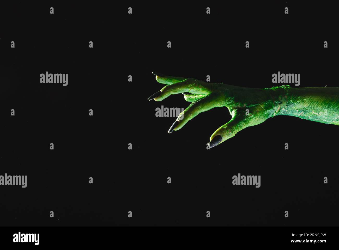 Mano mostro verde con unghie nere che raggiungono lo sfondo grigio Foto Stock
