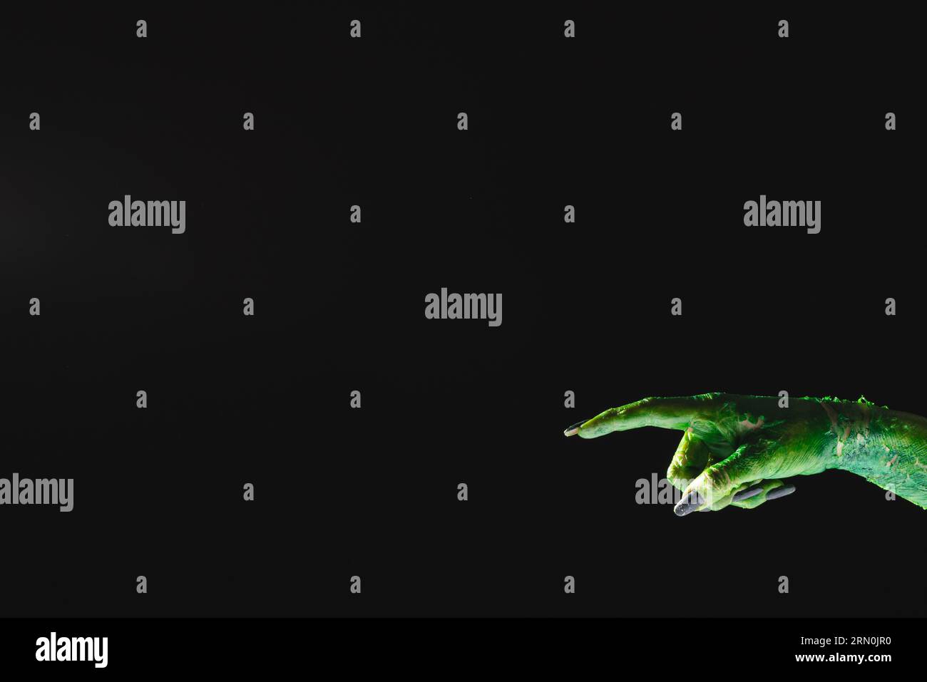 Mano mostro verde con unghie nere che puntano con il dito su sfondo nero Foto Stock