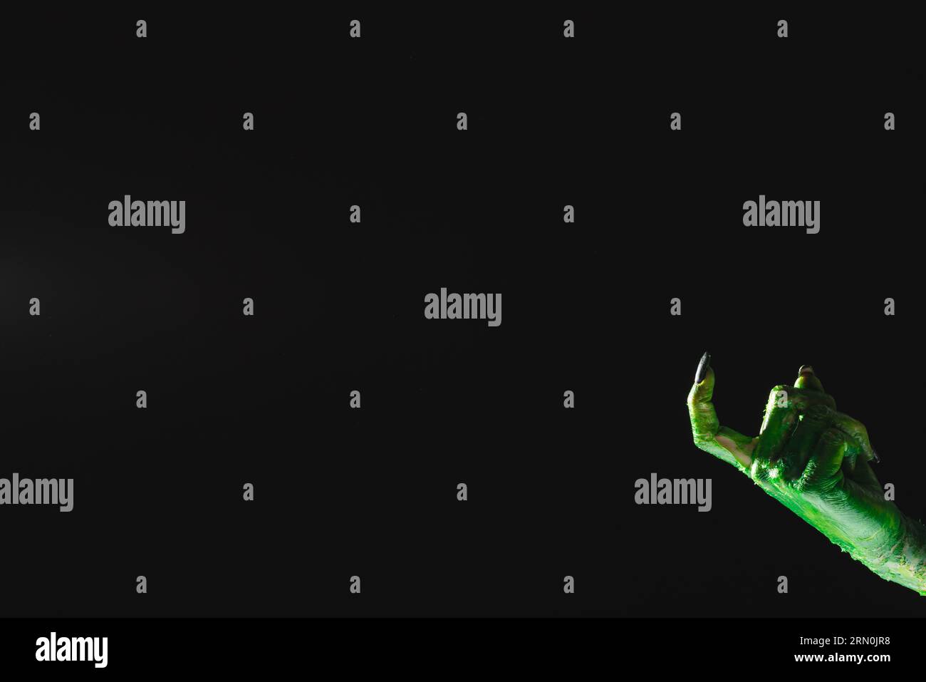 Mano mostro verde con unghie nere che puntano con il dito su sfondo nero Foto Stock