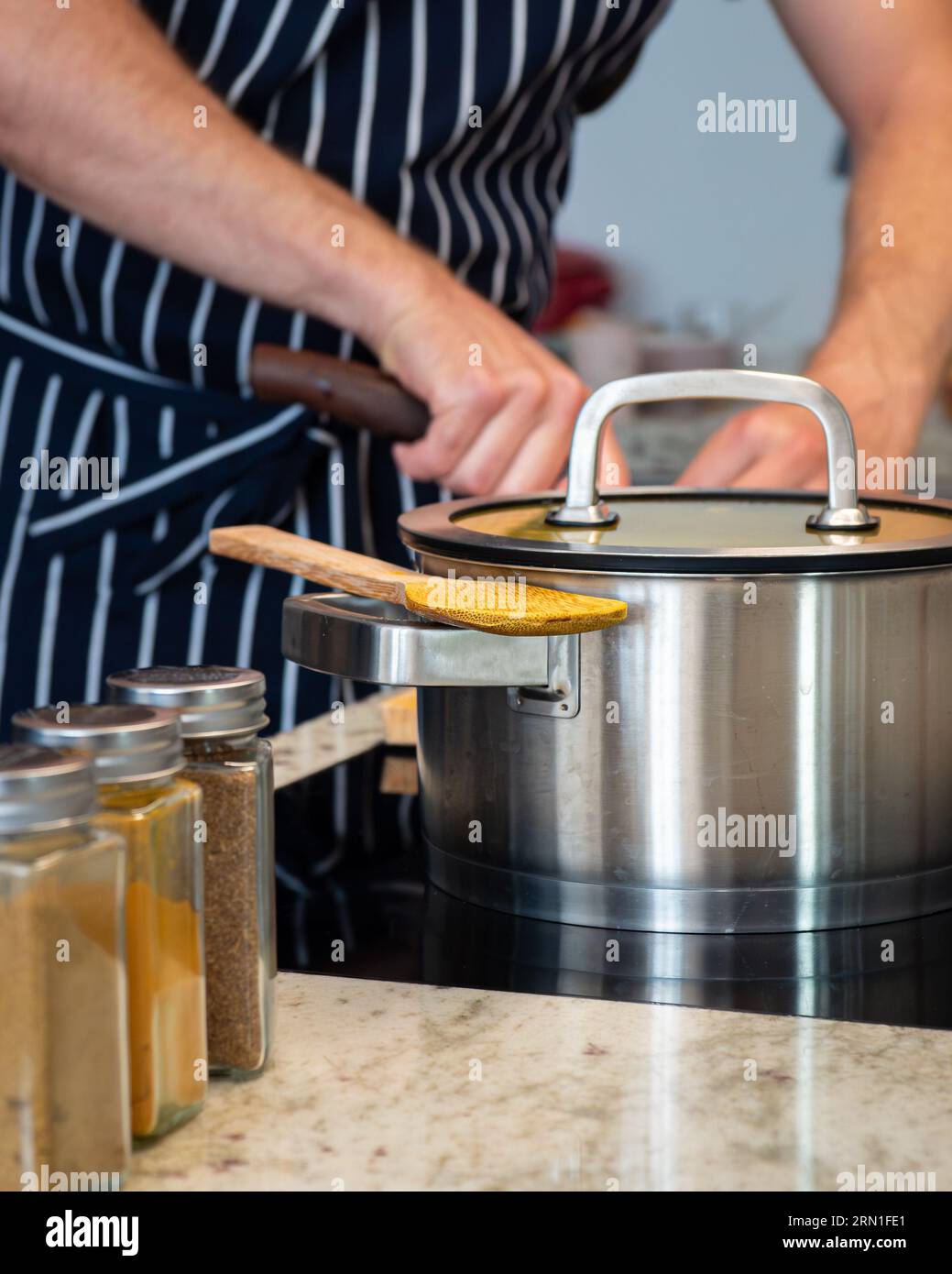 chef professionista in cucina durante la cottura con spezie, pentola, cucchiaio da cucina in legno e mani maschili utilizzando un coltello da cucina sullo sfondo Foto Stock
