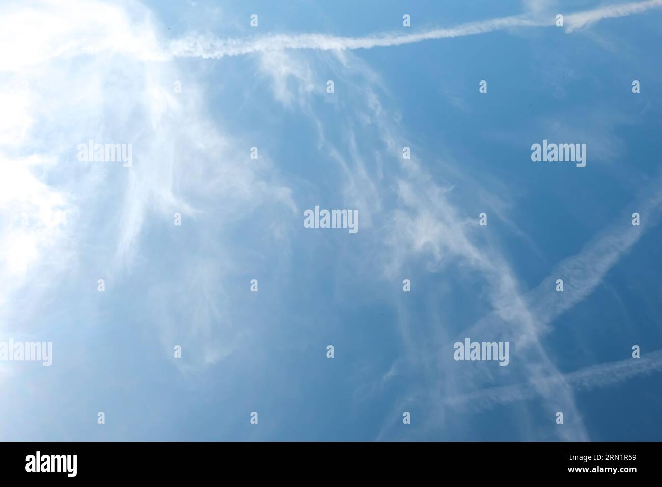 Nuvole di Cirrus e lunghe file di sentieri per aerei. L'aereo aeroplano si contraglia con lo sfondo blu del cielo nuvoloso. Linea orizzontale di volo aereo veloce in dista Foto Stock