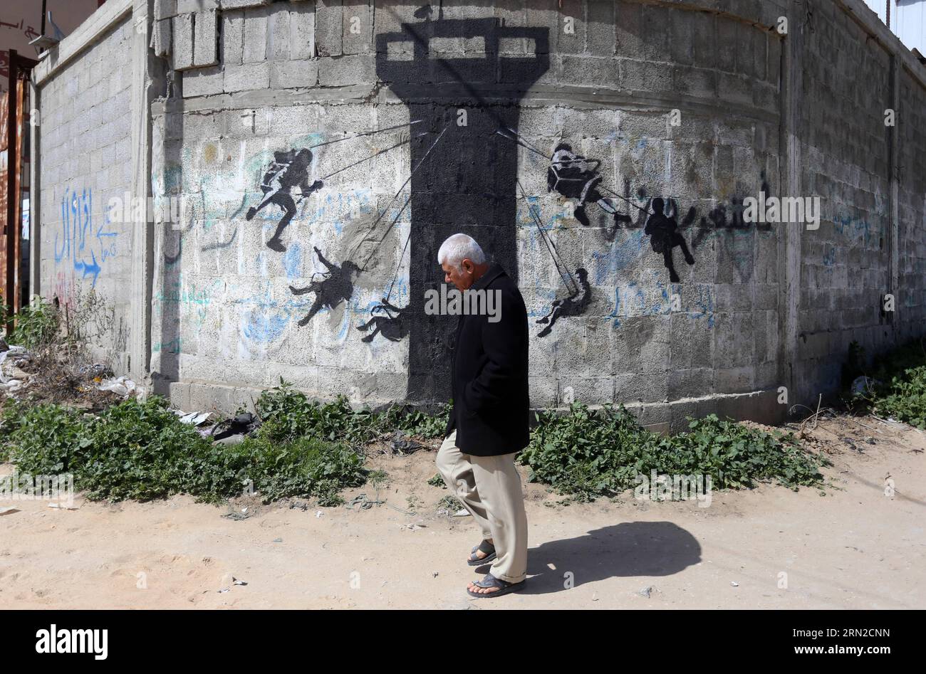 (150227) -- GAZA, 27 febbraio 2015 -- Un palestinese cammina davanti a un murale di bambini usando una torre di guardia dell'esercito israeliano come un giro in altalena, dipinta dall'artista di strada britannico Banksy, sui resti di una casa distrutta durante l'offensiva israeliana di 50 giorni sulla Striscia di Gaza negli ultimi luglio e agosto, nella città settentrionale di Beit Hanun, nella Striscia di Gaza, il 27 febbraio 2015.) MIDEAST-GAZA-MURALS-BANKSY YasserxQudih PUBLICATIONxNOTxINxCHN Gaza febbraio 27 2015 un PALESTINESE cammina davanti a un murale di bambini che usa la torre di guardia dell'esercito israeliano come un giro in slitta che ha dipinto il British Street Artist Banksy o Foto Stock